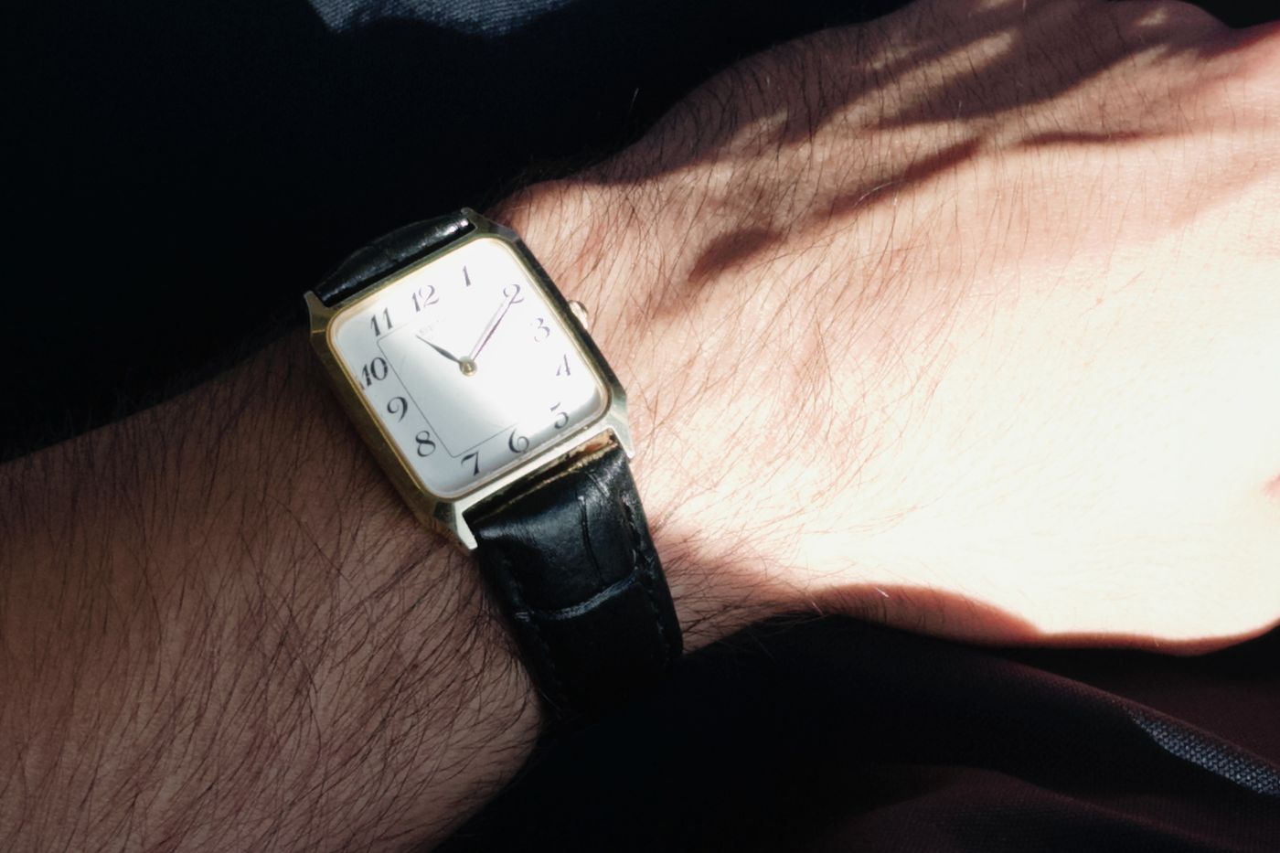 A vintage gold watch on a leather strap, worn on the wrist in low sunlight.