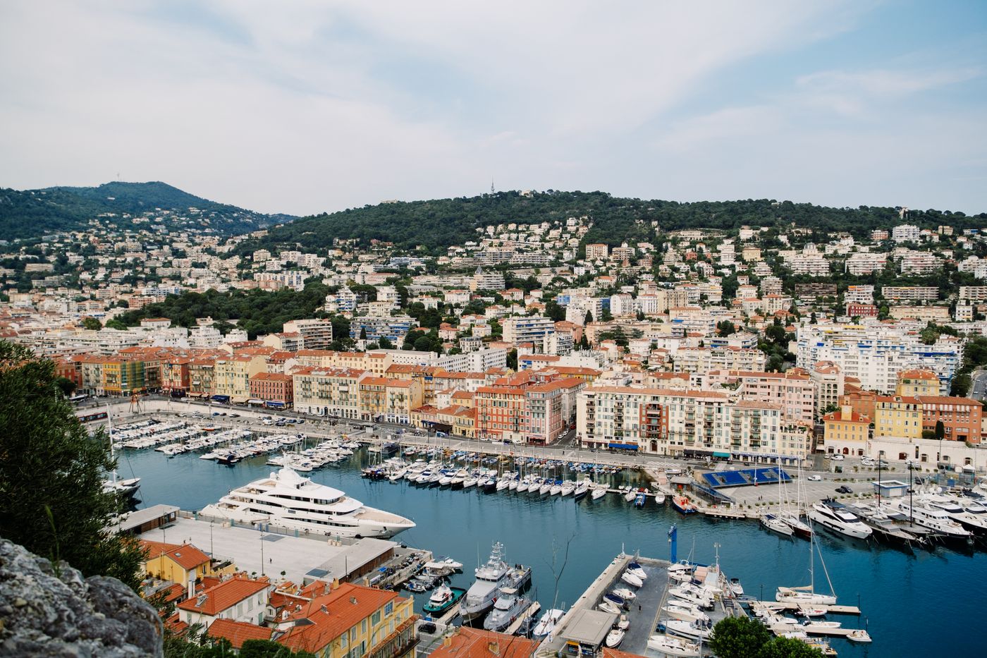 Le port de Nice, ses bateaux à quai et les collines derrière la ville.